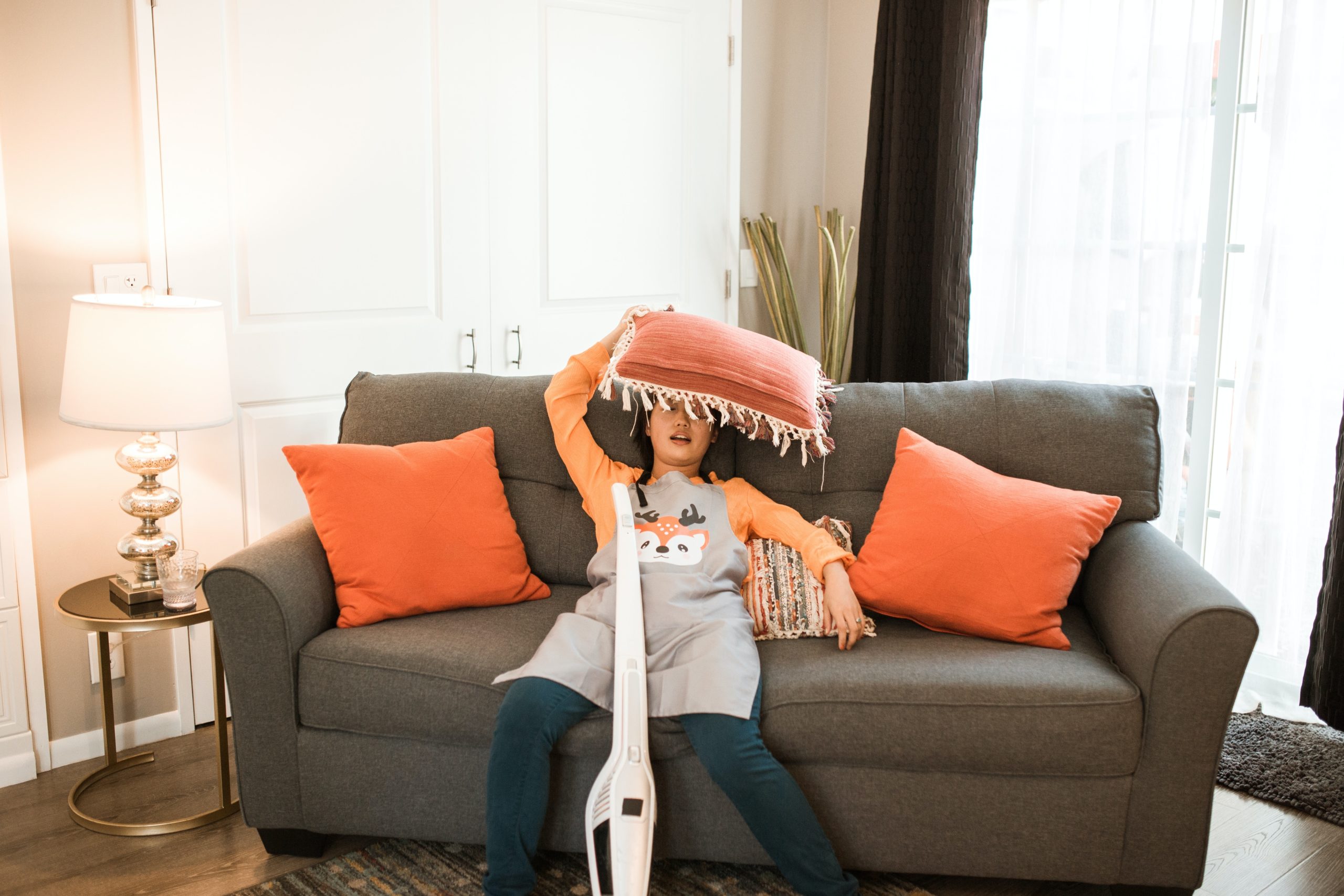 A woman sits on a sofa with a cushion on her head by the hoover, clearly not read our post on making cleaning fun!